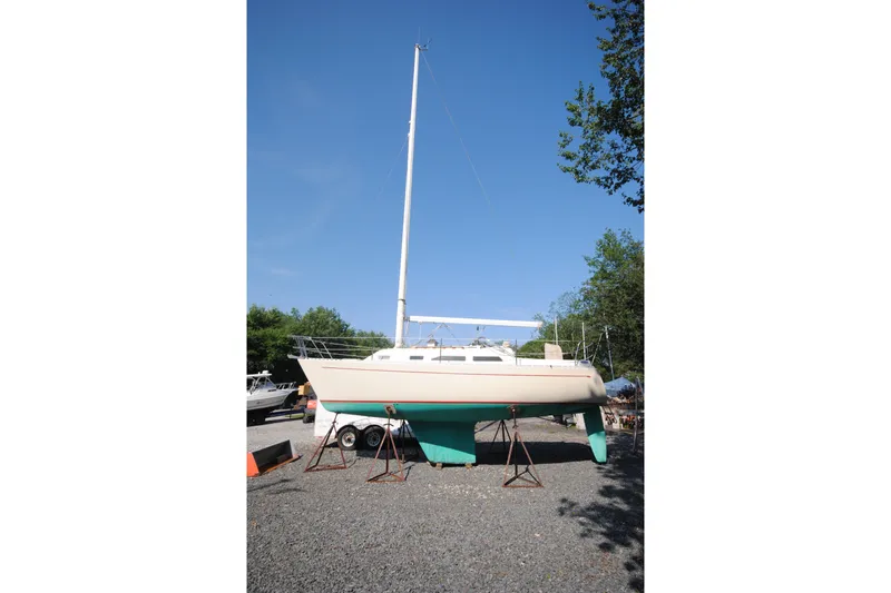 Slide: The Image of 1987 Tillotson-Pearson 28 sailboat on stands, clear sky, gravel lot. - 2