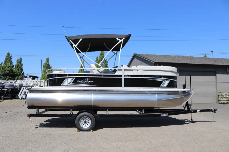 Slide: The Image of 2025 SunChaser Vista 20 Fish pontoon boat on trailer, parked outdoors under clear blue sky. - 1