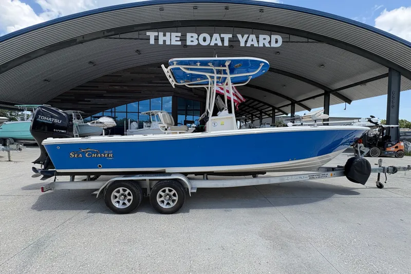 Slide: The Image of 2019 Sea Chaser 26 LX boat on trailer at dealership, featuring blue hull and Tohatsu engine. - 2