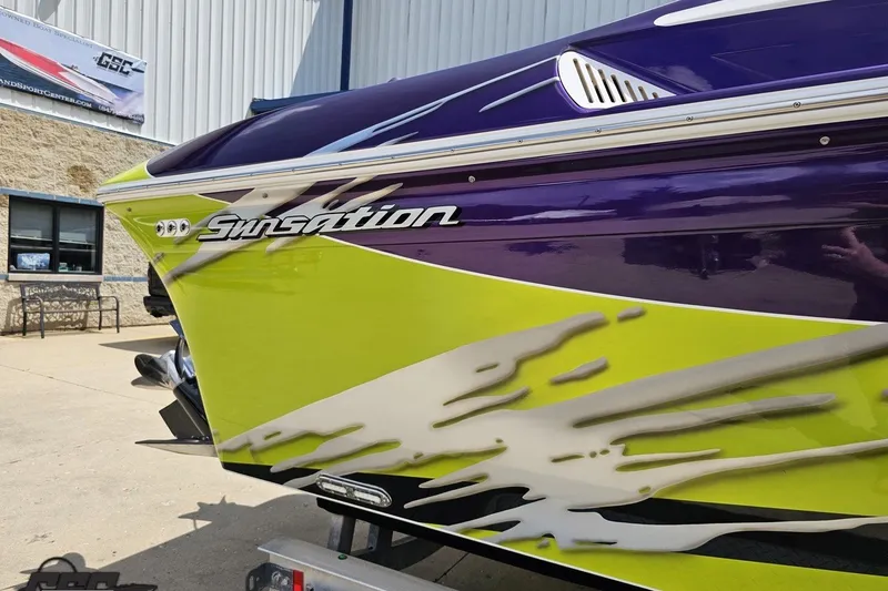 Slide: The Image of 2007 Sunsation 32 Dominator boat with vibrant green and purple design, docked outdoors. - 8