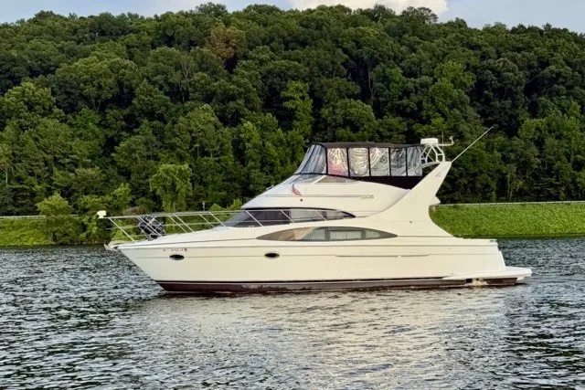Slide: The Image of 2004 Carver 420 Mariner yacht cruising on a serene lake with lush green forest backdrop. - 2