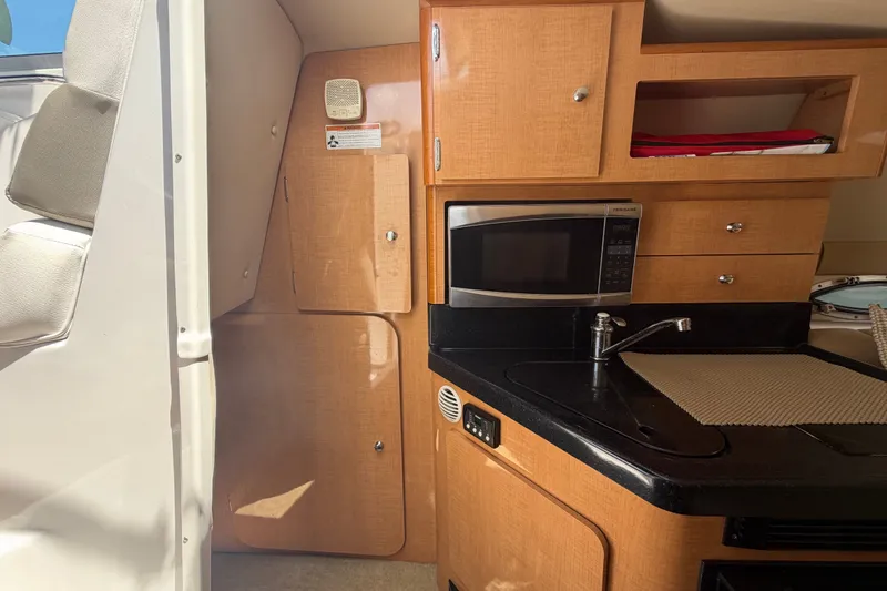 Slide: The Image of 2016 Glastron GS 259 boat interior with kitchenette, featuring microwave and sink. - 43