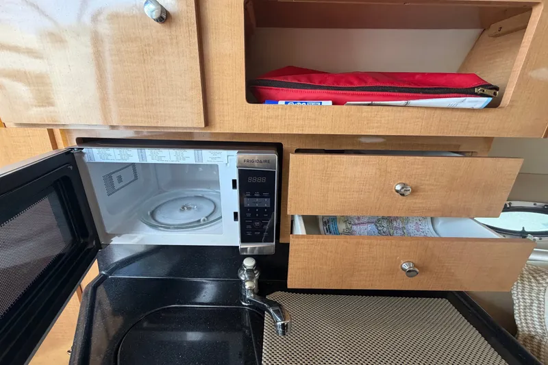 Slide: The Image of 2016 Glastron GS 259 interior kitchen with microwave, sink, and wooden cabinets. - 55