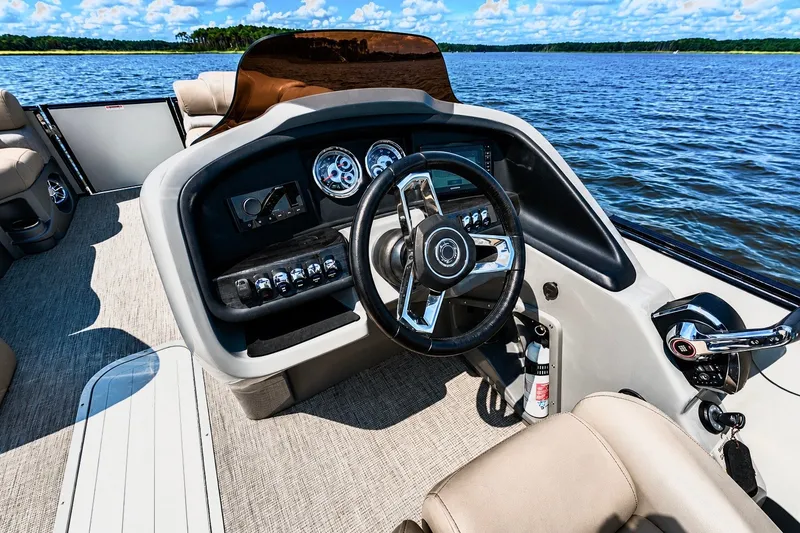 Slide: The Image of 2022 Avalon Catalina Platinum Quad Lounge boat interior with steering wheel and dashboard on a lake. - 6