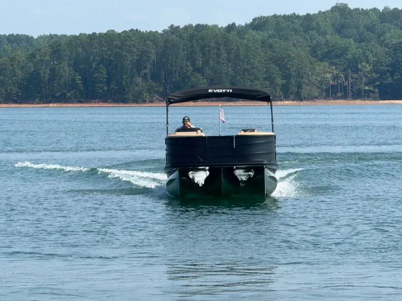 Slide: The Image of An Evotti 521QL pontoon boat cruising on a calm lake with a wooded shoreline in the background. - 3