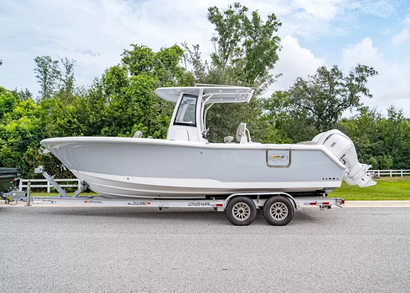 Slide: The Image of A 2027 Sea Hunt Ultra 265 SE boat on a trailer, surrounded by trees. - 2