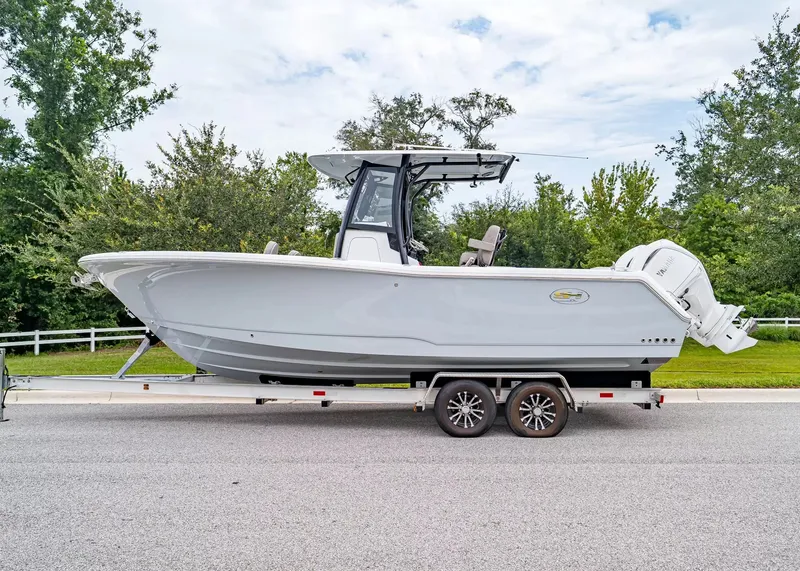 Slide: The Image of A 2026 Sea Hunt Gamefish 25 on a trailer, surrounded by trees and a fence. - 2