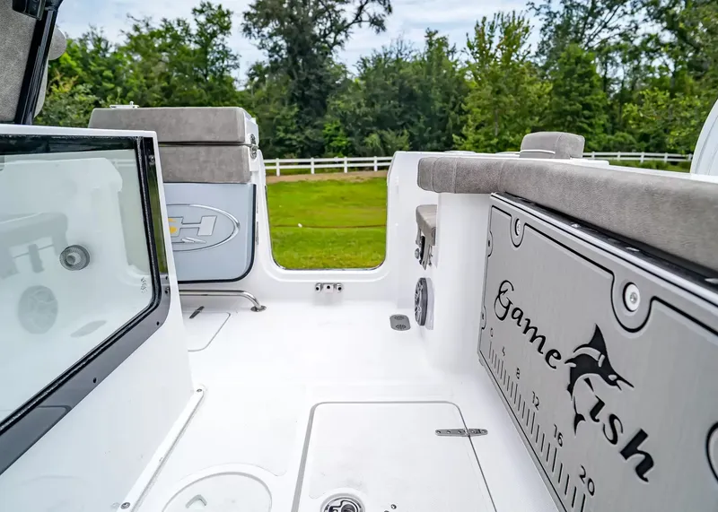 Slide: The Image of The image shows the cockpit of a Sea Hunt Gamefish 25 boat. It features a clean, white surface with gray upholstery and a measuring ruler on the floor. Trees and a fence are visible in the background. - 8