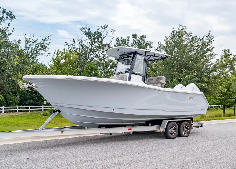 The Image of A 2026 Sea Hunt Gamefish 25 boat on a trailer on a road, surrounded by trees. - 1