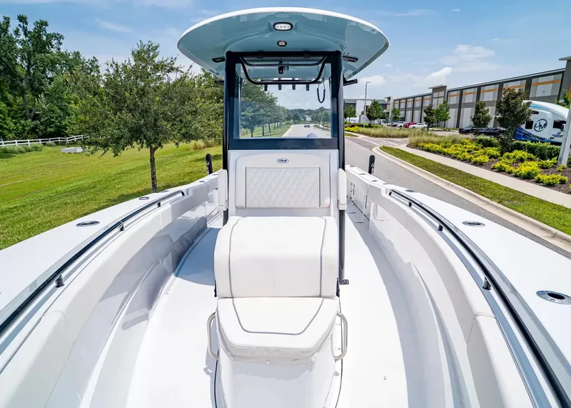 Slide: The Image of The image shows a 2027 Sea Hunt Gamefish 27 Coffin Box boat. It features a spacious deck with white upholstery and a modern helm. Trees and a building are visible in the background. - 23