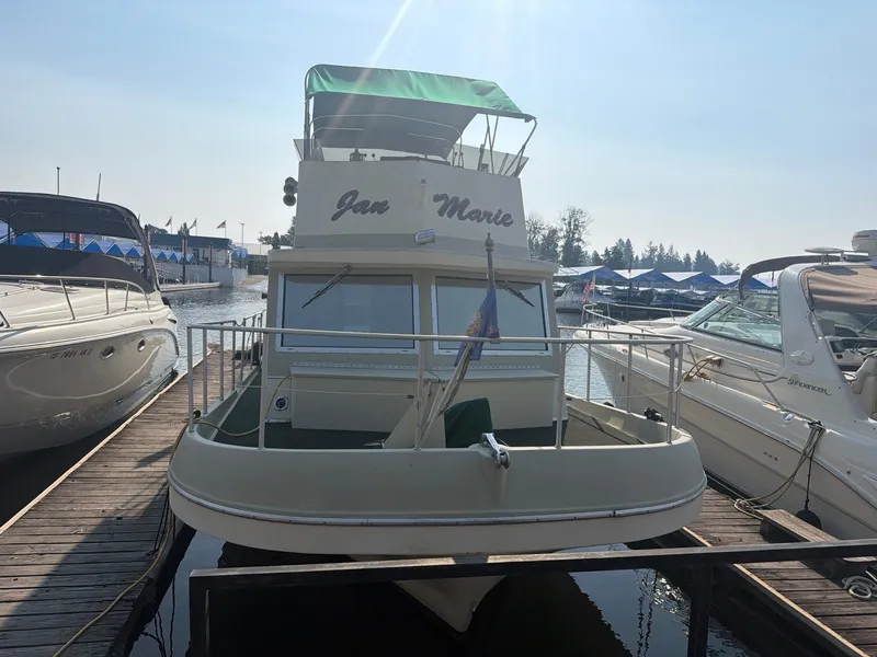 Slide: The Image of A 1977 Cruise-A-Home Corsair 40 with a green sunshade, docked between other boats. - 3