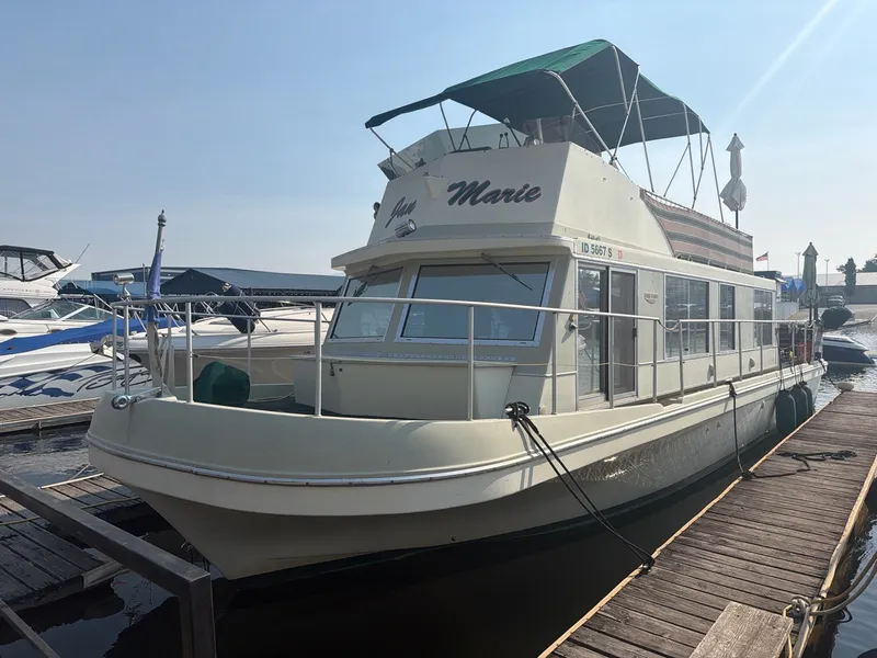 Slide: The Image of A 1977 Cruise-A-Home Corsair 40 houseboat docked. It features a spacious deck and a green sunshade. - 4