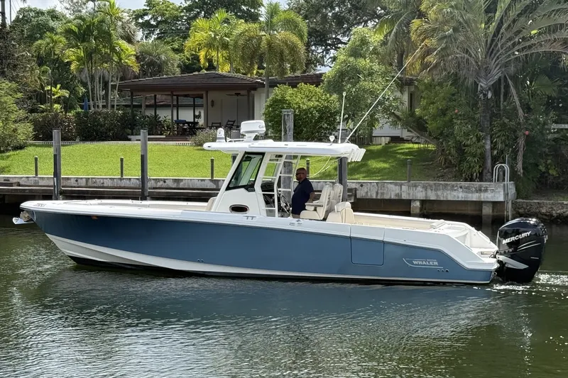 The Image of 2016 Boston Whaler 330 Outrage boat cruising on a calm waterway near lush greenery. - 0