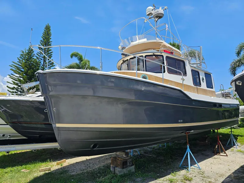 Slide: The Image of A 2014 Ranger Tugs 31-CB with a gray hull is on stands, surrounded by palm trees. - 2