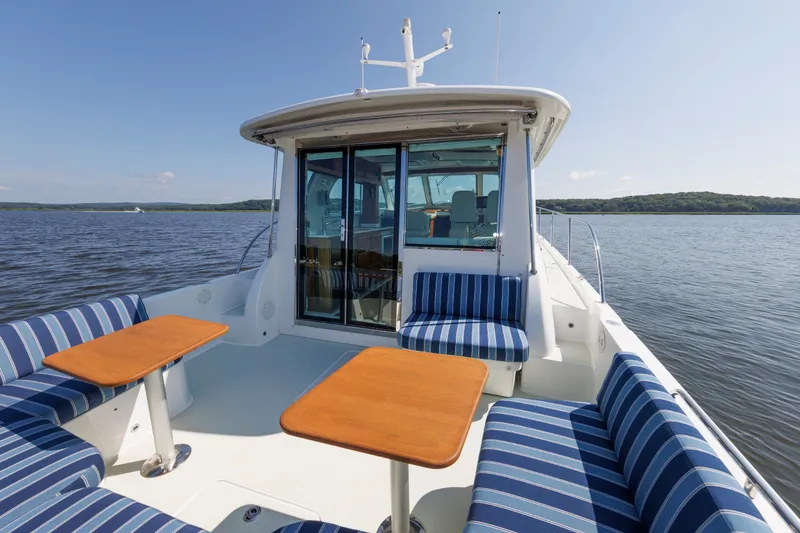 Slide: The Image of 2020 Back Cove 41 boat with striped seating and wooden tables on a calm lake. - 1