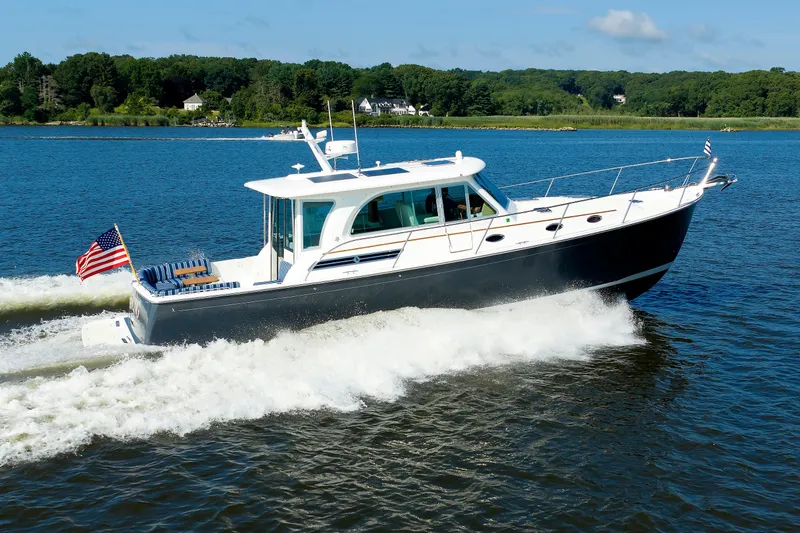 Slide: The Image of 2020 Back Cove 41 yacht cruising on a serene lake with lush green shoreline. - 54