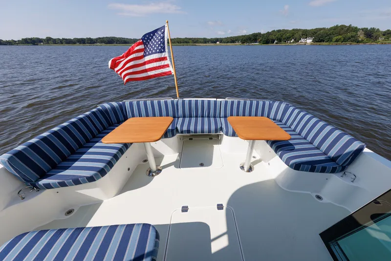Slide: The Image of Back Cove 41 (2020) boat deck with striped seating, tables, and American flag on a calm lake. - 39