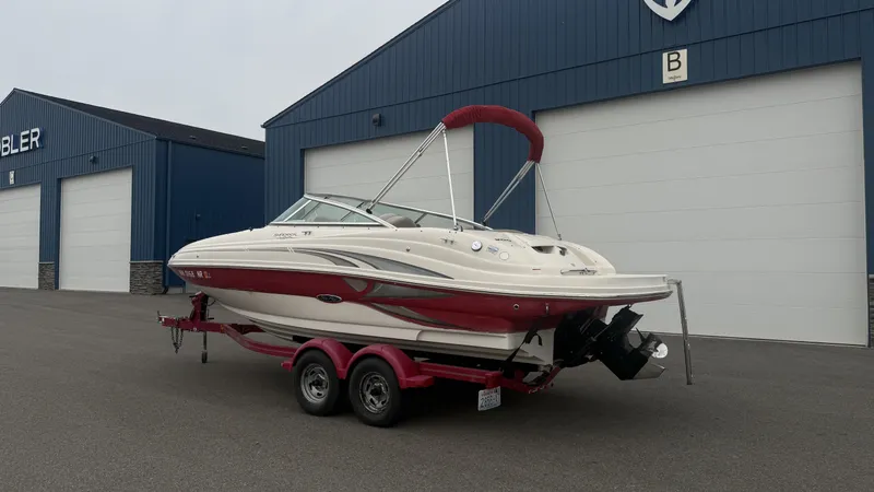 The Image of A white and red 2004 Sea Ray 200 Sundeck boat on a trailer in front of a blue building. - 1