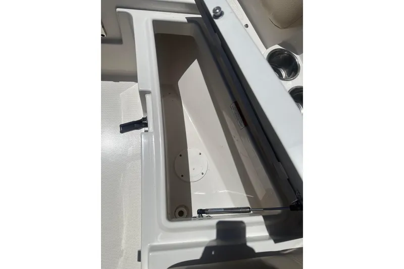 Slide: The Image of Open storage compartment on 2018 Sailfish 245 DC boat, featuring cup holders and latch mechanism. - 19