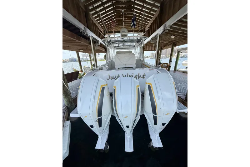 Slide: The Image of 2020 Intrepid 407 Cuddy boat with triple outboard engines docked under a wooden shelter. - 12
