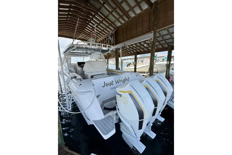 Slide: The Image of 2020 Intrepid 407 Cuddy boat docked with triple outboard engines under a wooden shelter. - 21