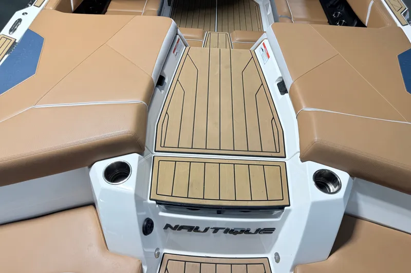 Slide: The Image of 2022 Nautique Super Air Nautique S23 boat interior with tan seating and teak flooring. - 23