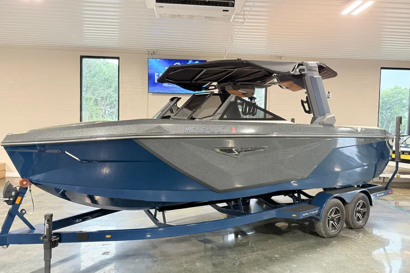 Slide: The Image of 2022 Nautique Super Air Nautique S23 boat in showroom, blue and gray design on trailer. - 7