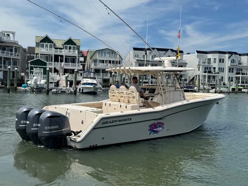 Slide: The Image of A 2016 Grady-White Canyon 336 boat navigates a harbor with modern buildings in the background. - 8