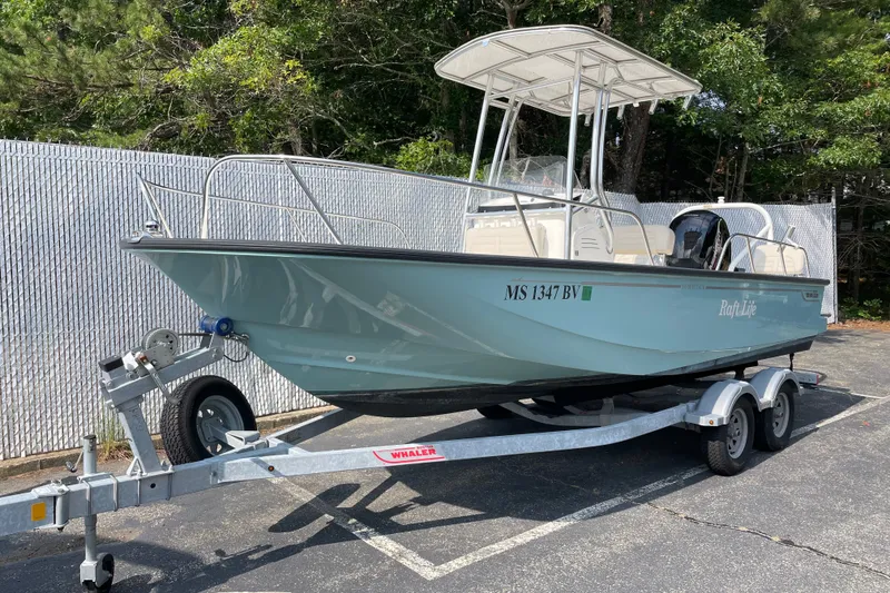 Slide: The Image of 2023 Boston Whaler 190 Montauk boat on trailer, parked outdoors with trees in background. - 2