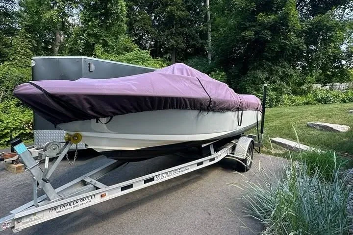 Slide: The Image of 2021 Edgewater 170CC boat covered on trailer, parked outdoors with lush greenery. - 4