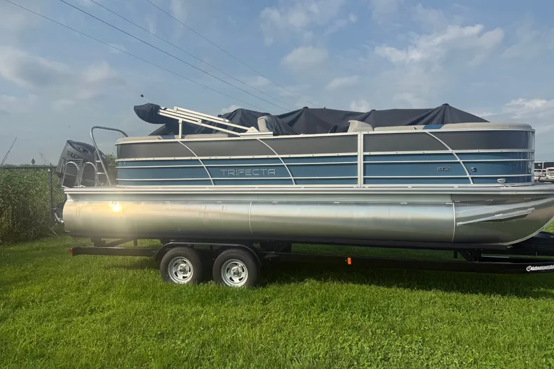 The Image of 2025 Trifecta 24 RF LE pontoon boat on trailer, parked on grass. - 1