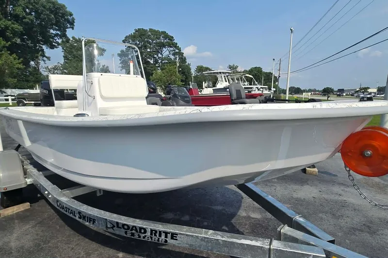 Slide: The Image of 2027 Coastal Skiff 171 boat on trailer, ready for transport, under clear blue sky. - 1