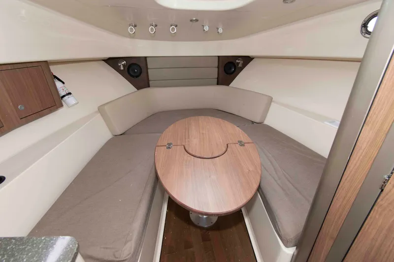 Slide: The Image of 2016 Boston Whaler 315 Conquest cabin interior with cushioned seating and wooden table. - 26