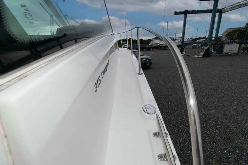 Slide: The Image of 2016 Boston Whaler 315 Conquest boat side view with railing and dock background. - 16