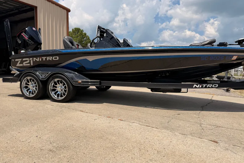 Slide: The Image of 2024 TRACKER NITRO Z21XL boat with sleek design and shiny wheels parked outdoors. - 1