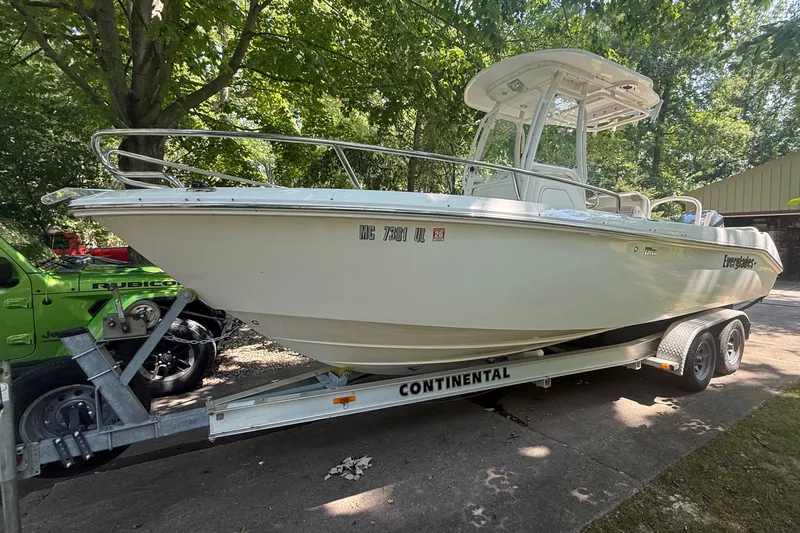 The Image of 2011 Everglades 230 Center Console boat on trailer, parked outdoors under trees. - 0
