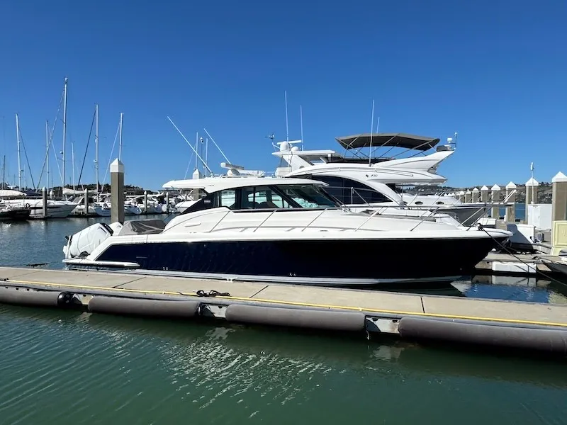 Slide: The Image of A 2022 Tiara Yachts 43 LE docked at a sunny marina, surrounded by other boats. - 2