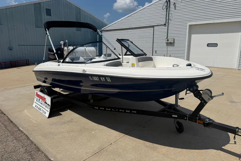 Slide: The Image of 2019 Bayliner 160 Bowrider boat on trailer, parked outside a marine dealership. - 1