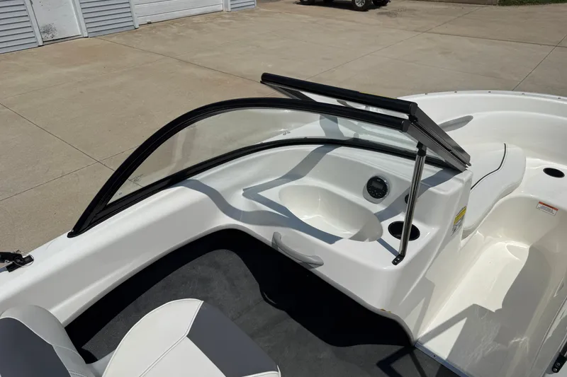 Slide: The Image of 2019 Bayliner 160 Bowrider interior with windshield and seating, parked on concrete. - 15
