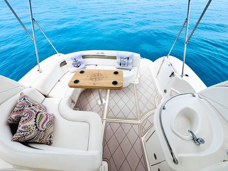 Slide: The Image of The image shows the stern of a 2006 Sea Ray 340 Sundancer. There's a cozy seating area with a wooden table and decorative pillows. The boat is on calm, blue water. - 15