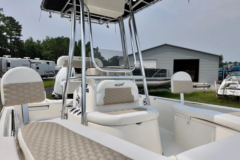 Slide: The Image of 2027 Bulls Bay 2200 XS boat with beige seating, parked near a metal building and RVs. - 12