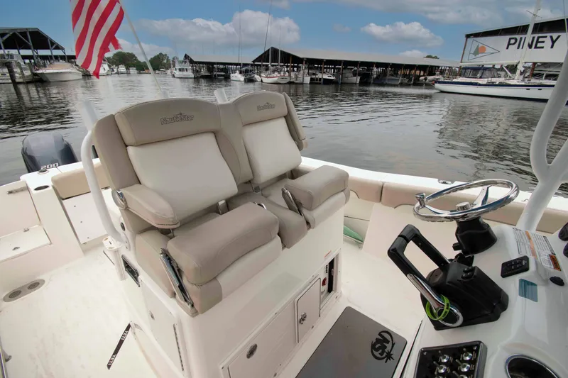 Slide: The Image of 2016 NauticStar 28 XS boat interior with helm, seating, and American flag at marina. - 2