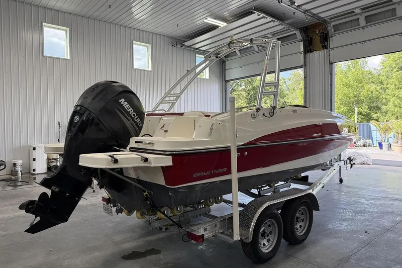 Slide: The Image of 2014 Bayliner 190 Deck Boat on trailer in a garage, featuring a Mercury outboard motor. - 1