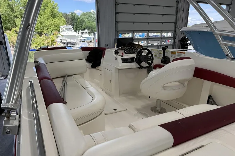 Slide: The Image of 2014 Bayliner 190 Deck Boat interior with white and maroon seating, steering console, and open garage view. - 6