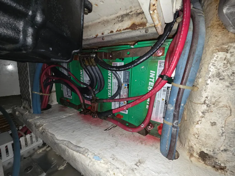 Slide: The Image of Batteries and cables in a boat engine compartment, surrounded by structural elements and hoses. - 26