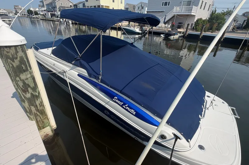 The Image of 2008 Crownline 240 LS boat docked, covered with blue canopy, in a serene waterfront setting. - 0