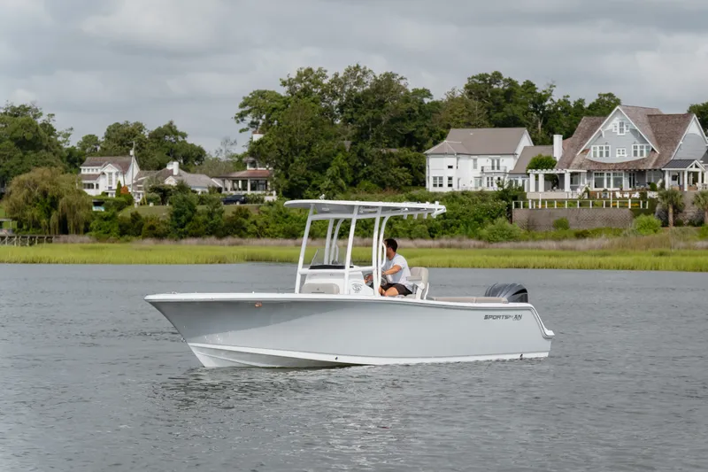 Slide: The Image of 2023 Sportsman Heritage 231 Center Console boat cruising on a serene lake near luxury homes. - 2