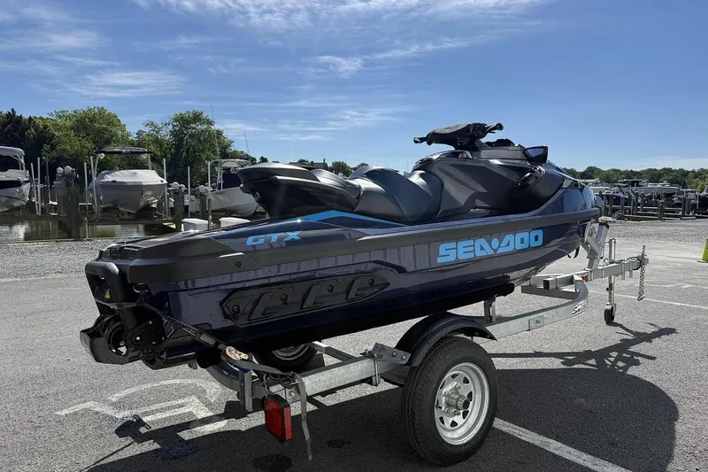 Slide: The Image of 2024 Sea-Doo GTX 230 jet ski on trailer, parked near marina under clear blue sky. - 2