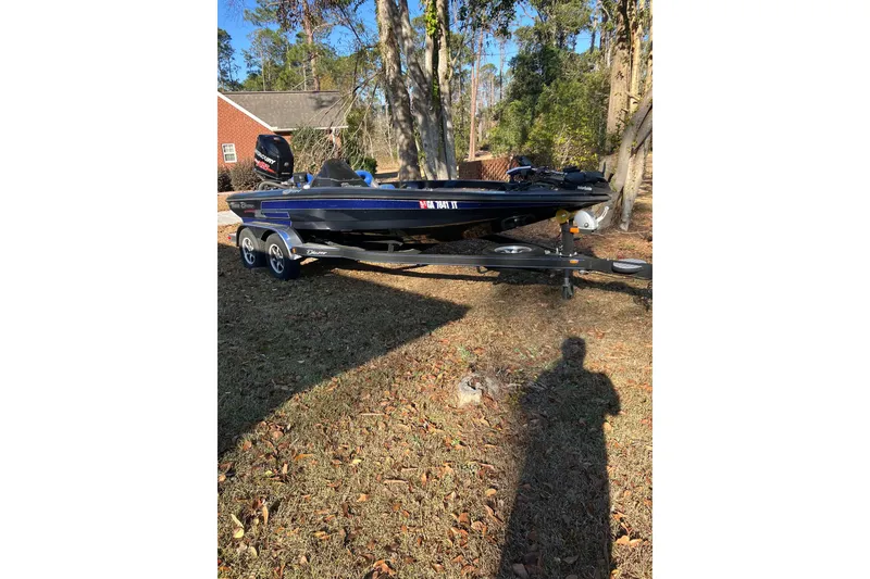 Slide: The Image of 2016 Blazer 202 Pro-V boat on trailer, parked outdoors near trees and a house. - 1