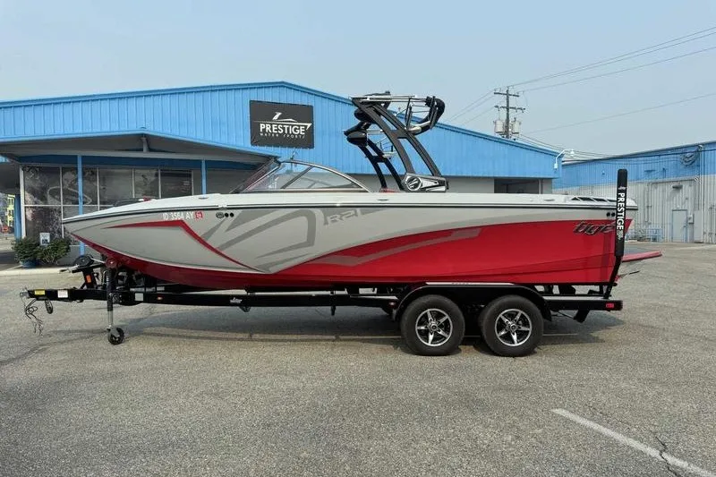 The Image of 2018 Tigé R21 boat on trailer outside Prestige dealership, red and gray design. - 1